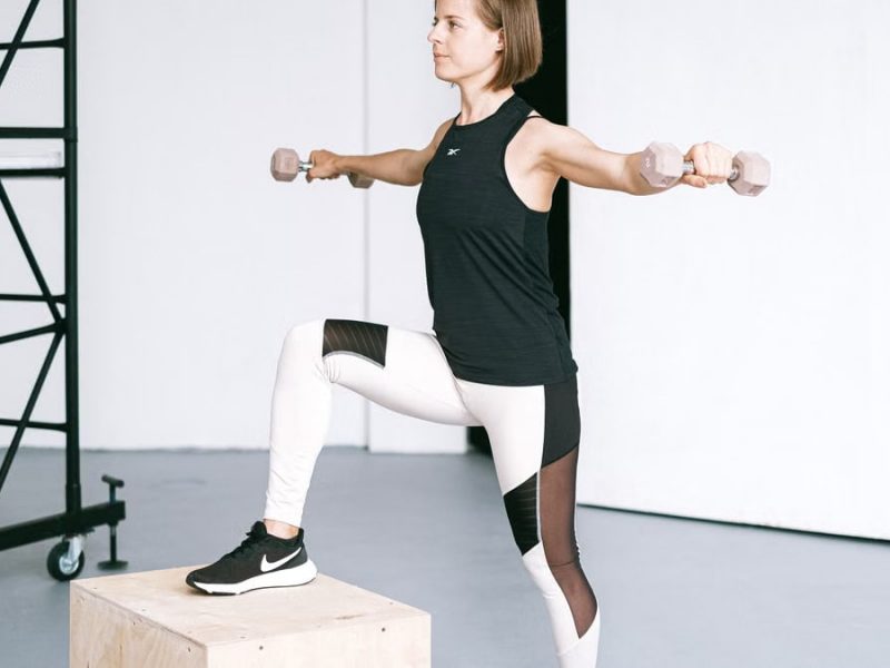 Woman performing fitness exercise with dumbbells in a gym setting, showcasing strength and balance.